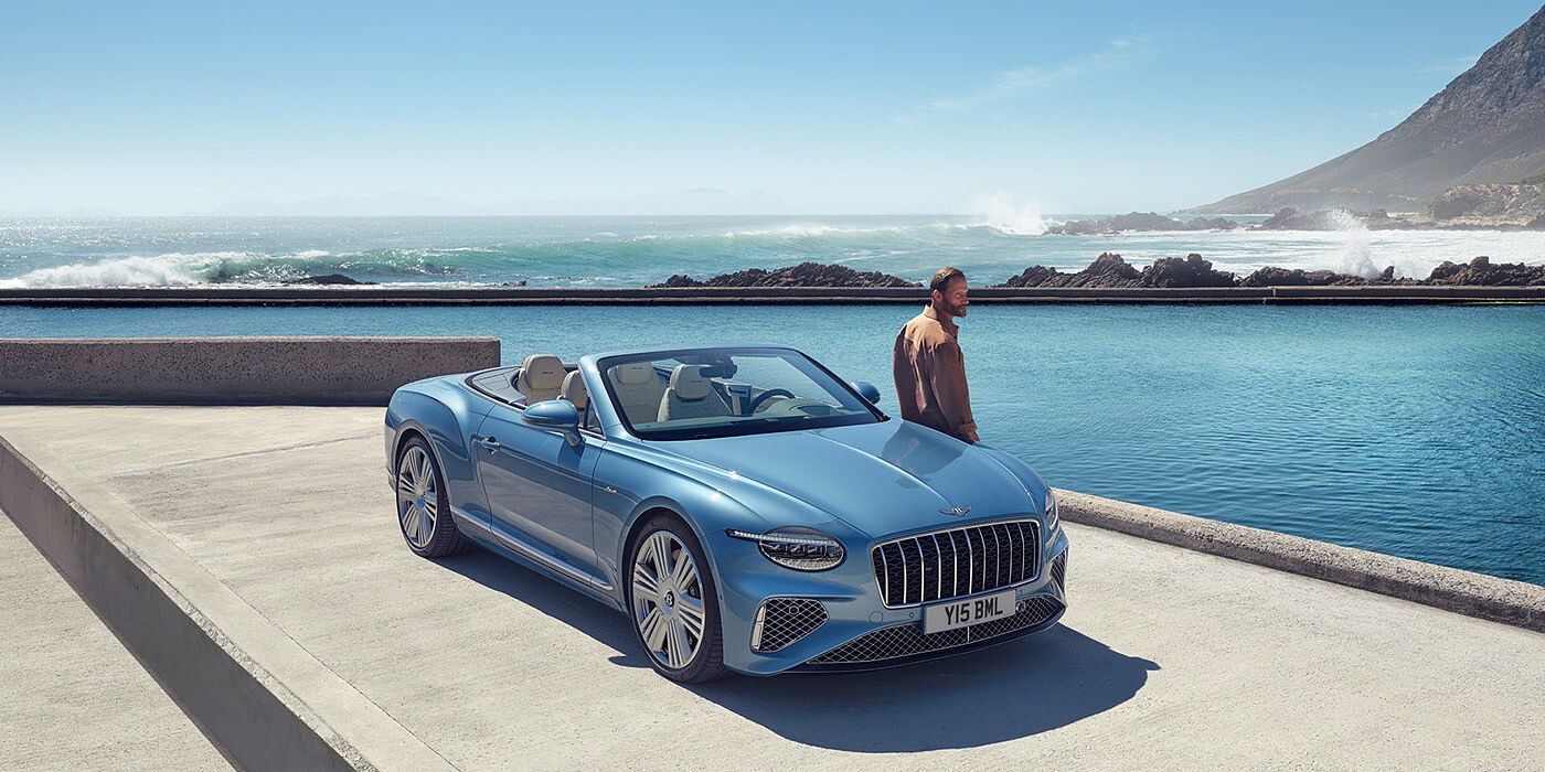Bentley Polanco New Bentley Continental GTC Azure convertible front view in Light Windsor blue paint with 22 inch ten spoke wheels parked by the sea in the sunshine