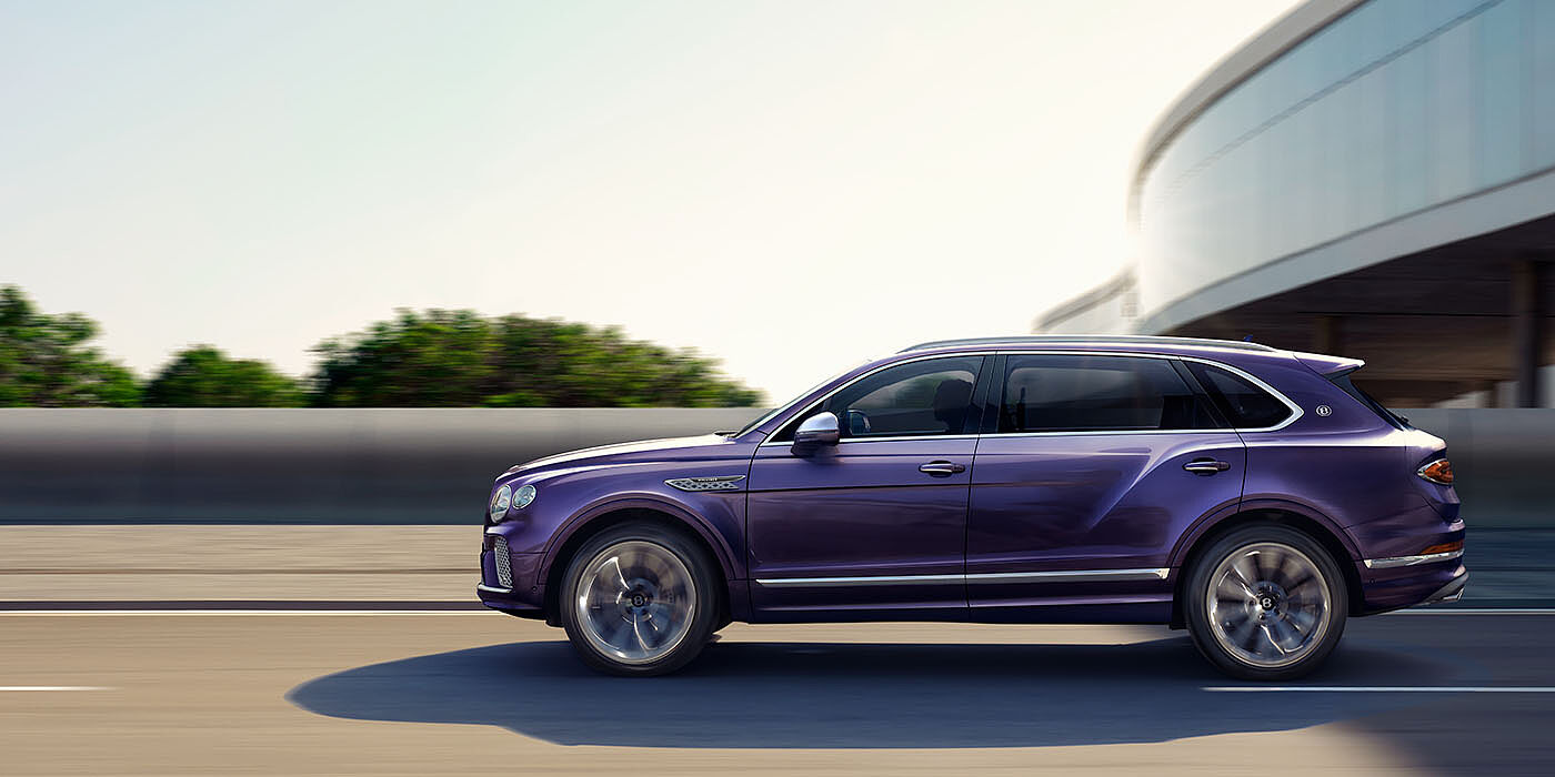 Bentley Polanco Bentley Bentayga Extended Wheelbase Mulliner luxury SUV profile in Tanzanite Purple paint, driving on an country road past trees.