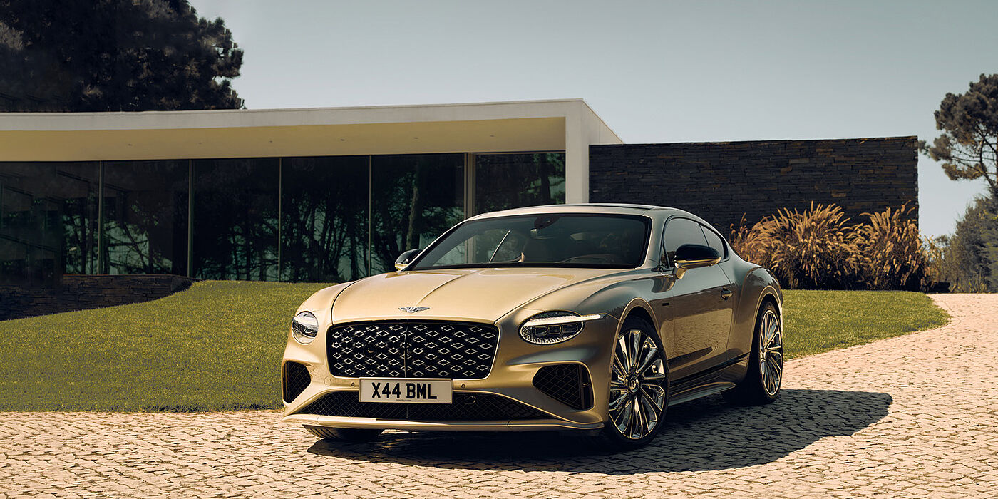 Bentley Polanco Bentley Continental GT Mulliner coupe front three quarters in Patina paint parked outside a glass fronted building with a grass lawn behind it