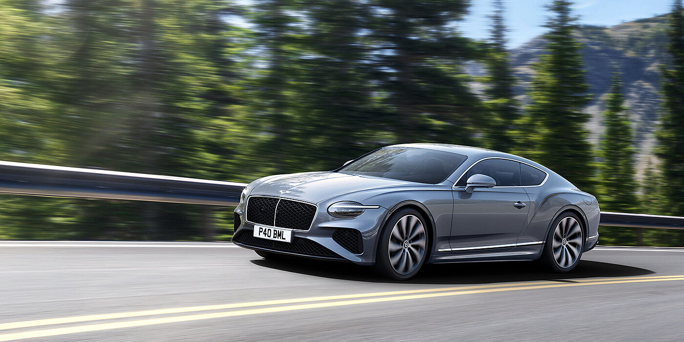 Bentley Polanco New Bentley Continental GT coupe in Silverlake paint and 22 inch ten-spoke wheels, driving dynamically on a tree-lined road in the sunshine