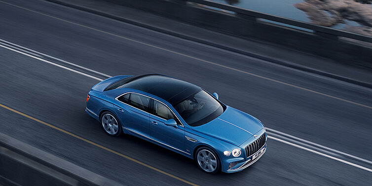 Bentley Polanco New Bentley Flying Spur Azure sedan in Light windsor blue paint by Mulliner, with 22 inch Azure wheels seen from overhead driving dynamically on a country road