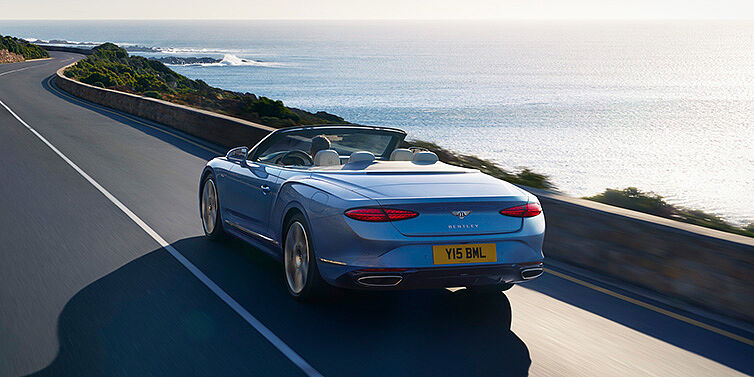 Bentley Polanco New Bentley Continental GTC Azure convertible rear view in Light Windsor blue paint with 22 inch ten spoke wheels driving dynamically on an ocean road in the sunshine