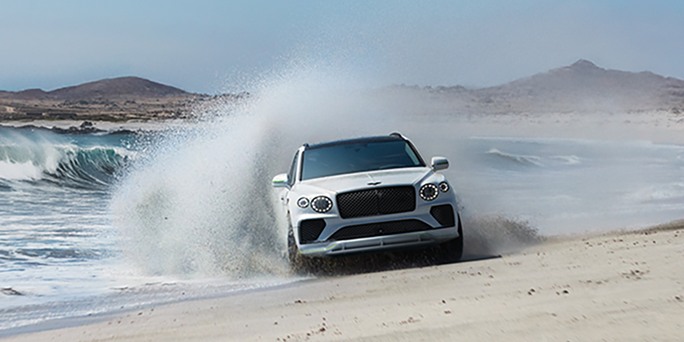 Bentley Polanco Bentley Bentayga Speed SUV facing front in Snow Quarts Pearlescent white paint driving dynamically on beach
